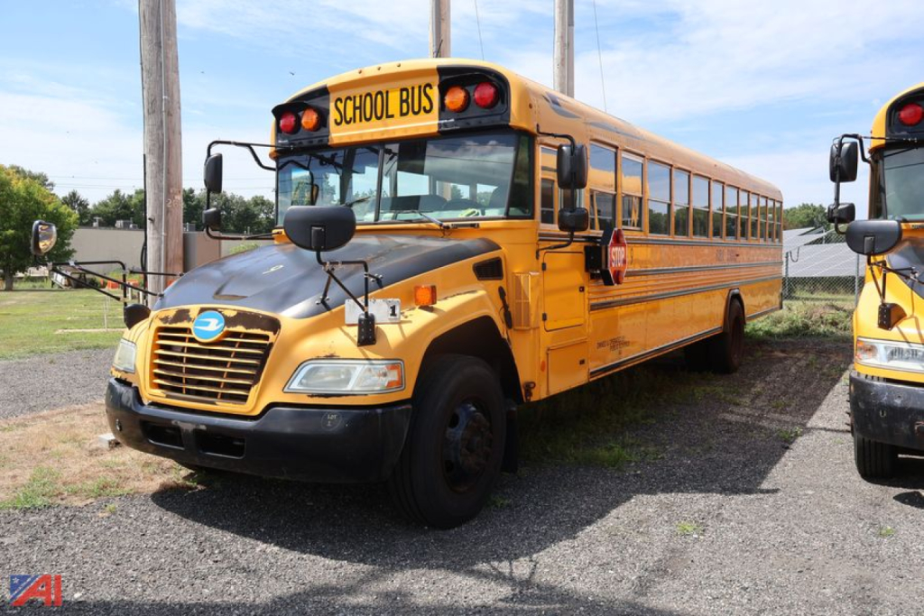 School bus in yellow/blue color showing front grille, headlights, side mirror, with 'SCHOOL BUS' sign on top and 'Blue Bird' emblem on hood.
