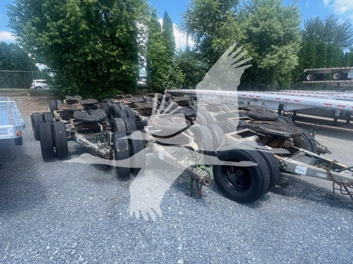 Trailer dolly chassis showing multiple axles and wheels with tires, winches, and metal frame; faint watermark of overlapping hands across image.