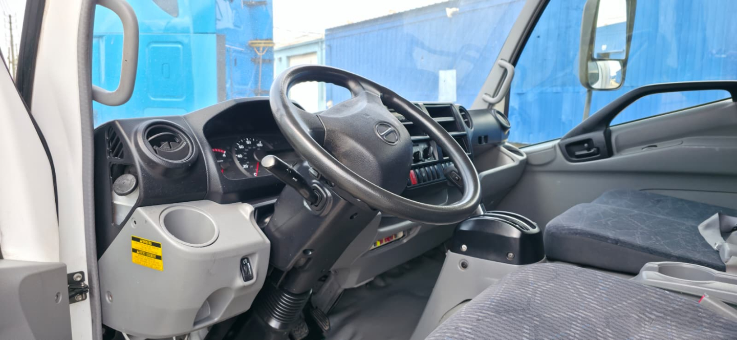 Truck cab interior with steering wheel and dashboard of a 2019 Hino 155, right-hand drive? showing instrument cluster, steering wheel, and gray seats.