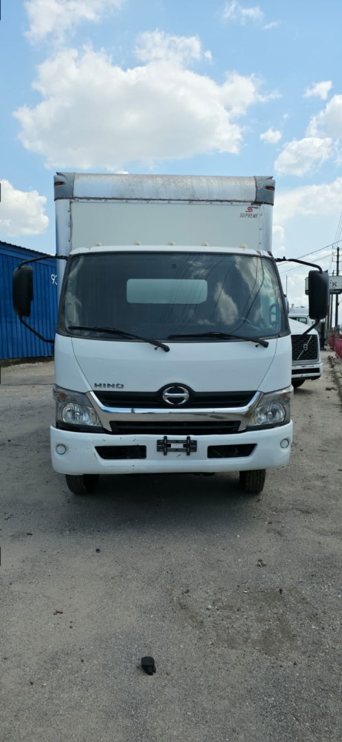 Front view of a 2019 Hino 155 box truck showing windshield, headlights, grille, and cab; white exterior with cargo box above.
