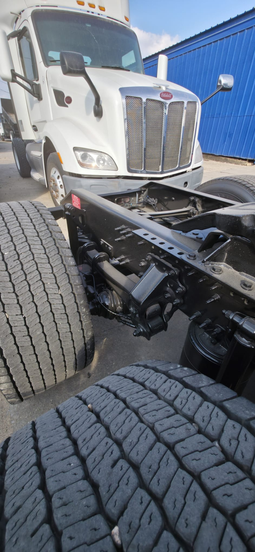 Truck chassis and front wheel area with a white 2019 Hino 155 cab visible in background, showing the engine bay view, dual rear wheels, and front suspension components.