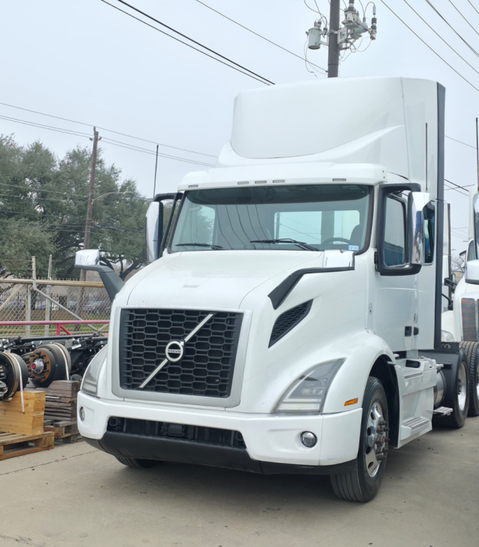 Truck cab in front view with Volvo-style grille on white 2019 Hino 155 box truck, aerodynamic bumper, mirrors, and high roof sleeper cab.