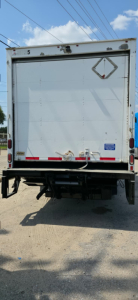 Rear view of a used 2019 Hino 155 box truck showing back doors, bumper, and diamond-shaped reflective sign on the door.