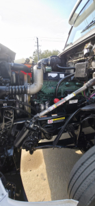 Engine bay of a 2019 Hino 155 box truck showing engine components, hoses, and belts from a side view.