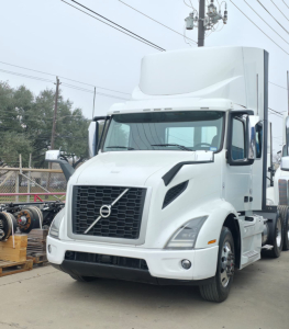 Truck cab in front view with Volvo-style grille on white 2019 Hino 155 box truck, aerodynamic bumper, mirrors, and high roof sleeper cab.