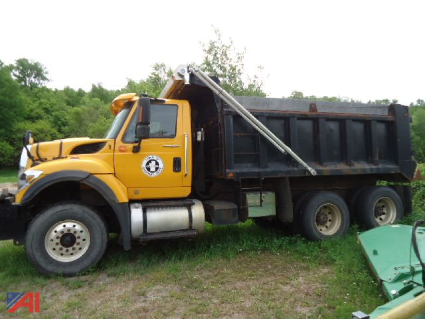 Dump truck side view showing yellow International WorkStar 7600 with black dumping bed and hydraulic hoist, on grassy lot.