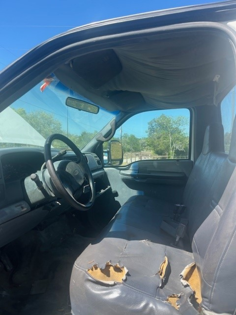 Interior view of a 2000 Ford F550 cab and chassis showing damaged front bench seat with torn upholstery, steering wheel, dashboard, and window in the background.