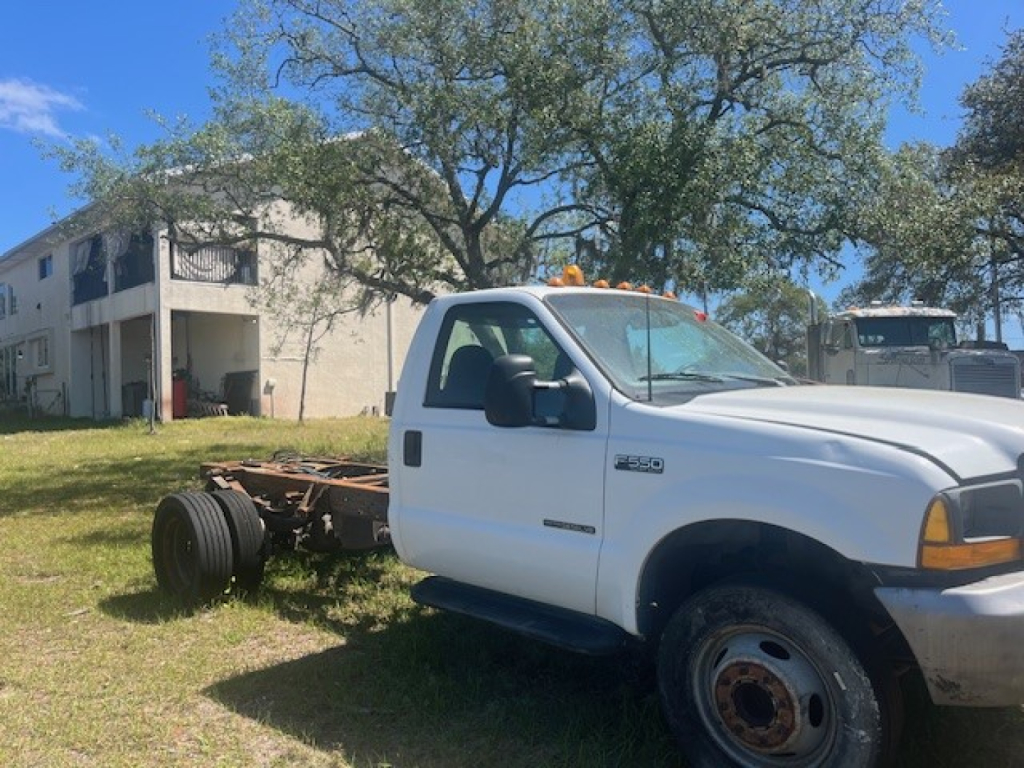 Ford F-550 cab and chassis in profile view showing front cab and exposed chassis rear with dual rear wheels, orange clearance light on roof, white body, black mirrors.
