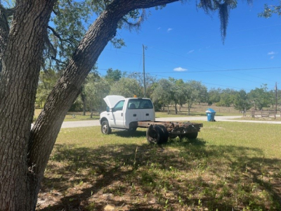 Ford F-550 cab and chassis truck with hood open in a grassy field; rear chassis visible with empty flatbed and wheel hubs.
