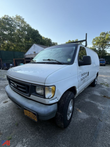 Ford E-250 cargo van with ladder rack on roof, front-left view, white exterior, NY registration plate, lettering on door