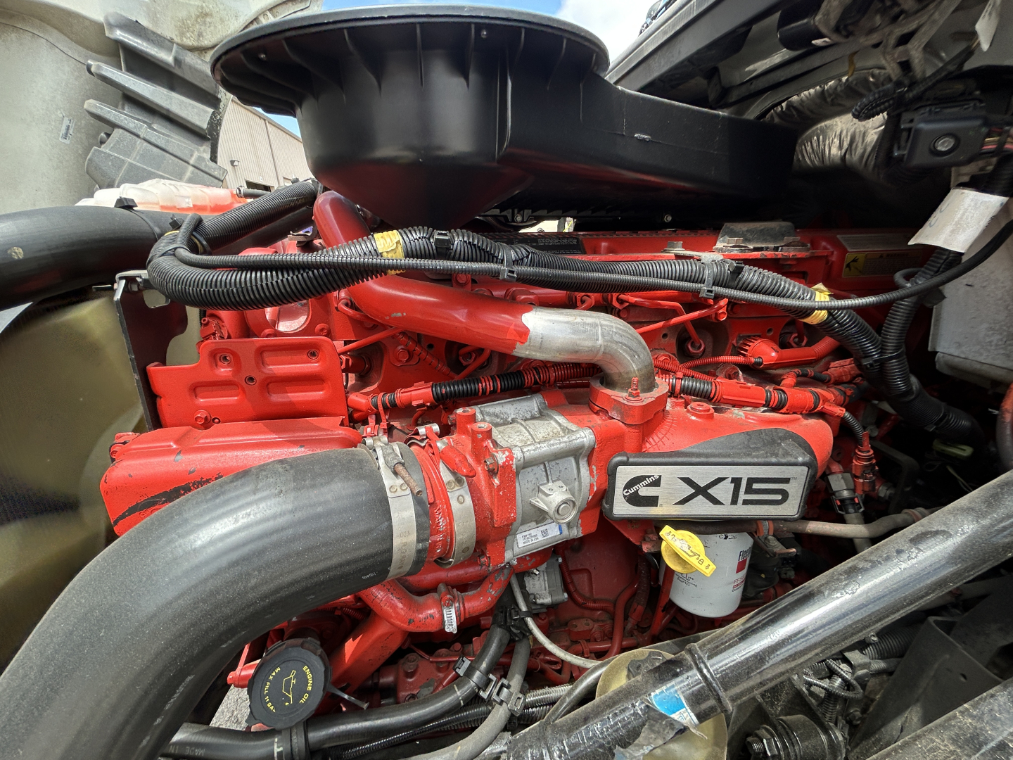 Engine compartment of a 2021 International LT625 truck showing a red engine with X15 badge, large intake tube, hoses, and yellow dipstick