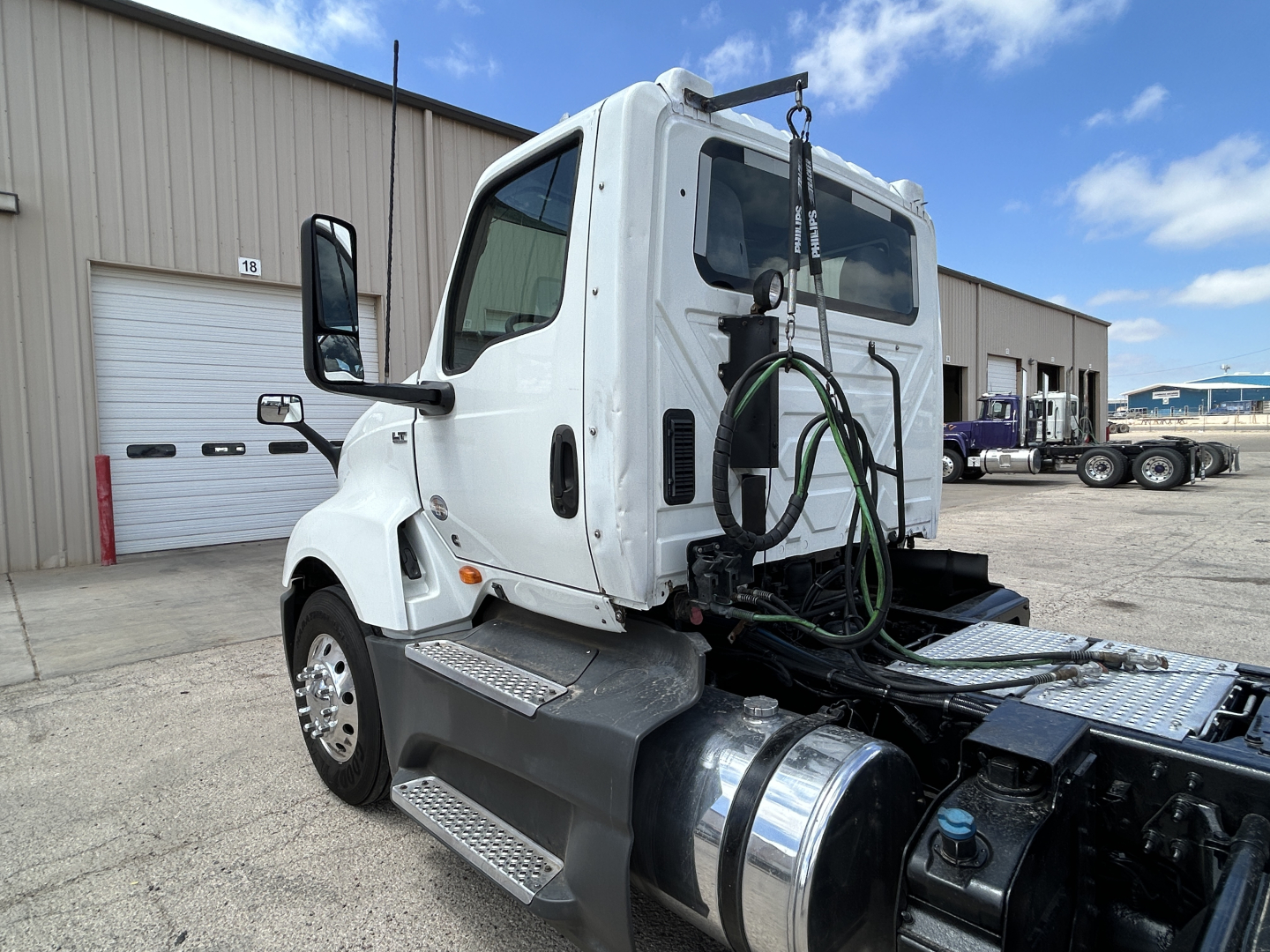 Truck cab and chassis of a 2021 International LT625 daycab with fuel tanks and hydraulic hoses visible at rear, diagonal view from left rear, chrome fuel tanks and steps present.