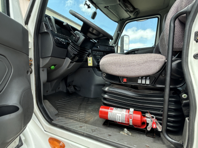 Truck cab interior showing driver's seat, steering wheel, and floor with a red fire extinguisher mounted near the door sill.
