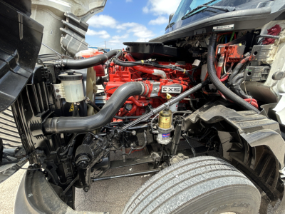 Truck engine bay showing Cummins X15 engine with red block, hoses, radiator, and various components.