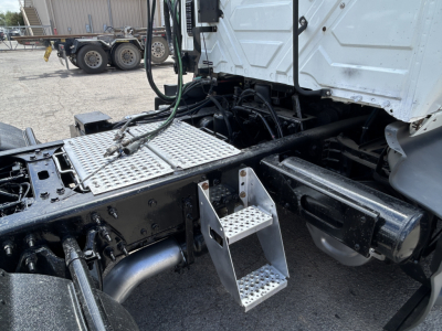 Truck cab and chassis of a 2021 International LT625 with metal diamond-plate steps, dual exhaust, and visible hydraulic lines in a parking yard.