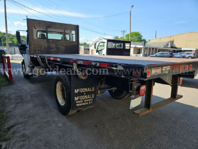 Flatbed tow truck in a yard showing rear and side, Freightliner M2 106 flatbed with branding and rear equipment.