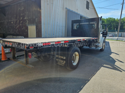 Freightliner M2 106 flatbed truck rear view showing dual rear wheels and flatbed deck.