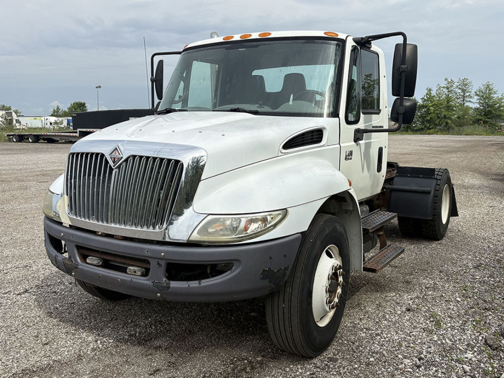 International 4400 conventional daycab truck front-left view showing grille, headlights, and cab with side mirrors; white cab and black bumper; chassis visible in background