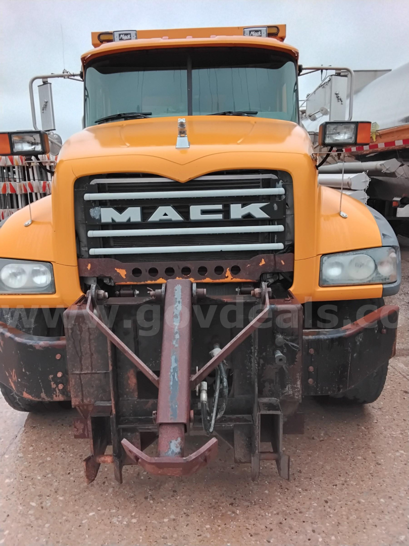 Front view of a yellow Mack GU713 dump truck with a large grille that reads MACK; front bumper and attachment equipment visible; headlights on either side.