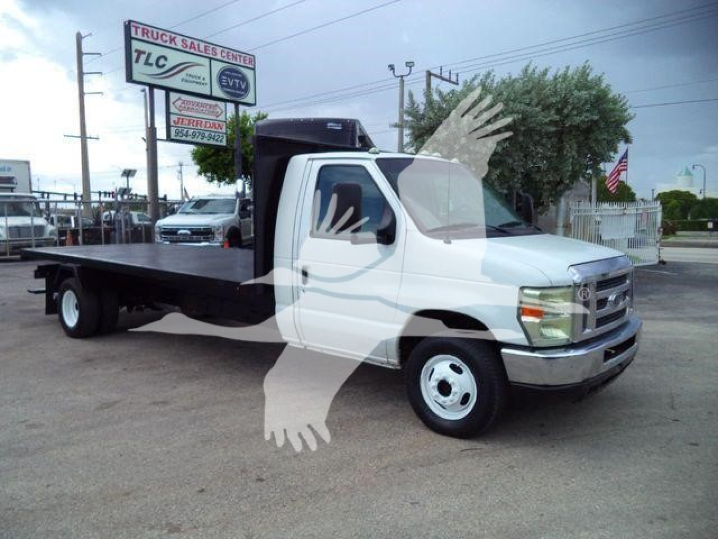Flatbed tow truck 2011 Ford E450 in white with a long flatbed, cab shot from passenger side, dealership lot in background