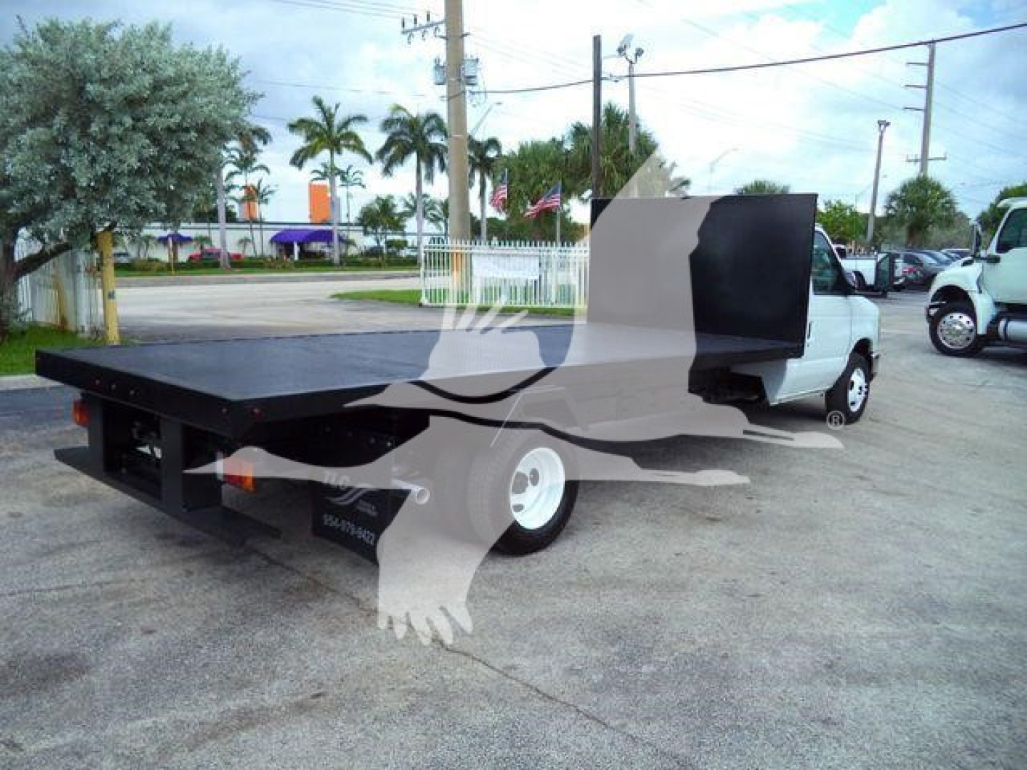 Flatbed tow truck with extended black bed and white cab, Ford E450, side view.