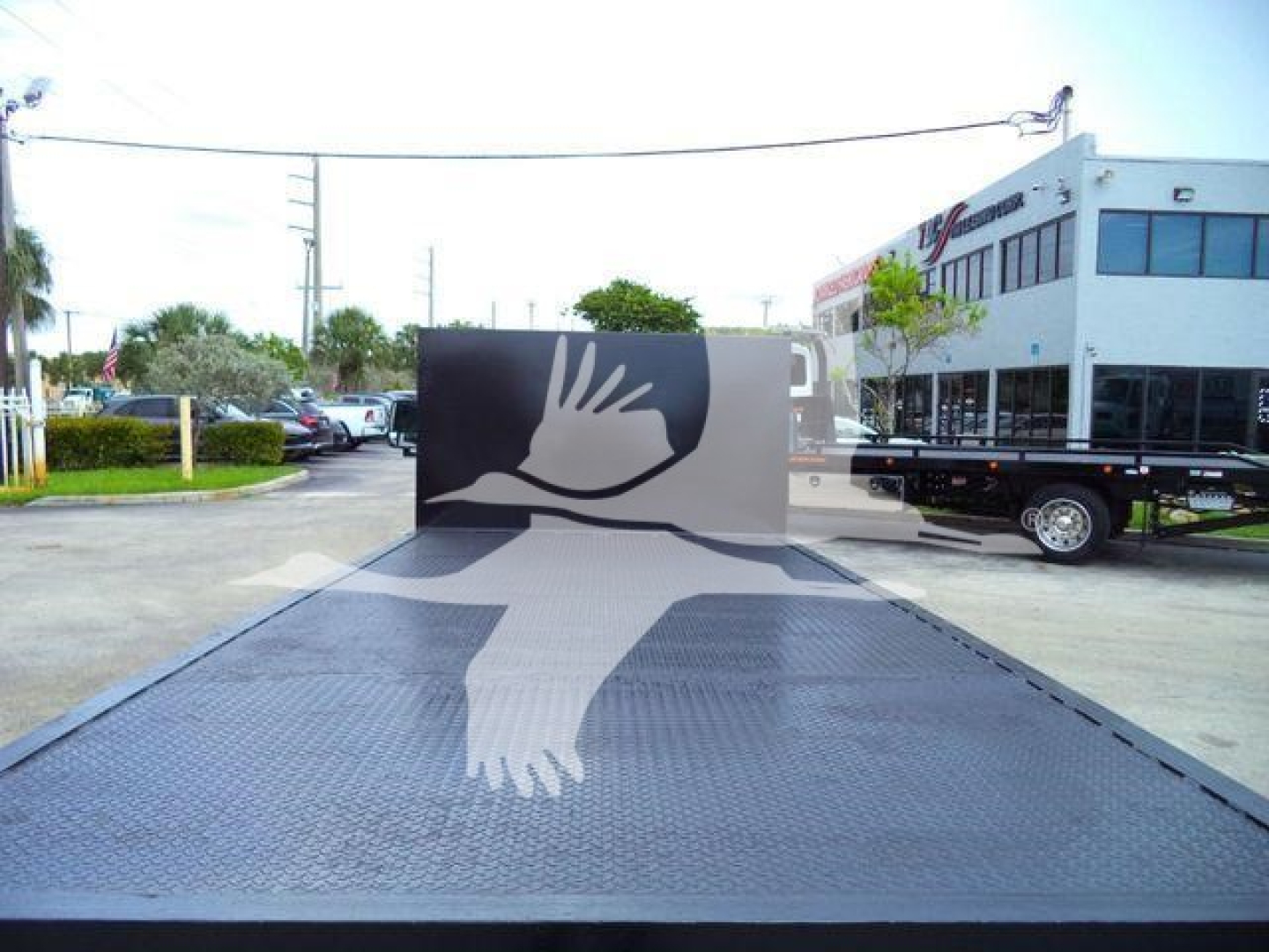 Ford E-450 flatbed truck in a dealership lot, stock number T07531FM, aluminum diamond plate flatbed with a large bird graphic on the rear crosspiece.