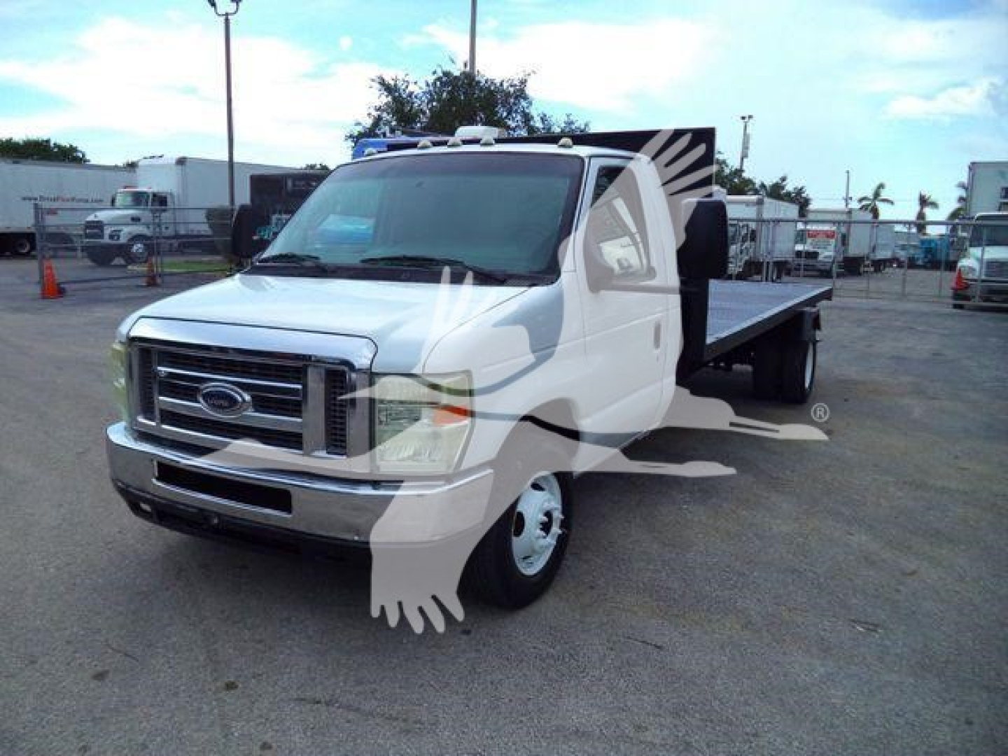 Ford E-450 flatbed truck in a dealership lot, side view showing flatbed and cab with Ford grille.