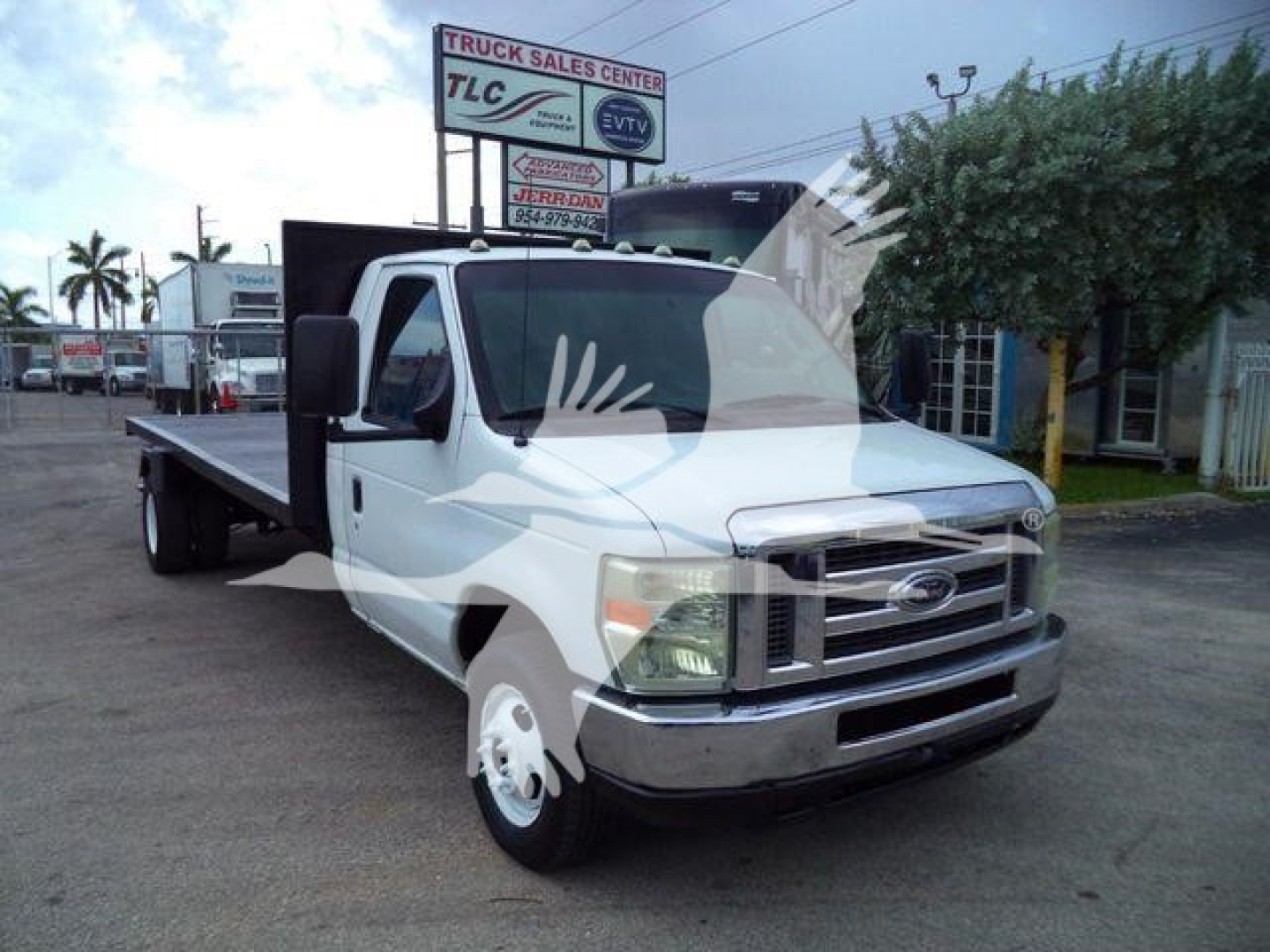 Flatbed Ford E-450 truck in a dealership lot showing a flatbed cargo bed and cab with Ford emblem; background includes dealership signage.