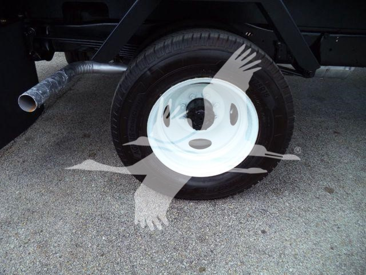 Ford E-450 flatbed truck wheel and exhaust visible, single rear wheel with white steel rim and tire, part of chassis and exhaust pipe.