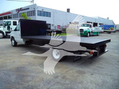 Flatbed tow truck in a lot with a long flatbed and a cab; no visible text on the truck body.