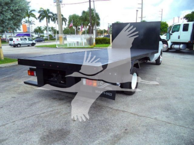 Flatbed tow truck rear view showing large flatbed with black toolbox and dual rear tires.