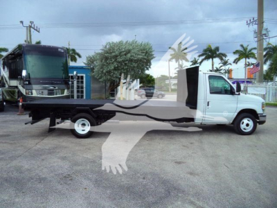 Side view of a white Ford E-450 tow bed flatbed truck with extended flatbed and black equipment on rear, parked in lot.