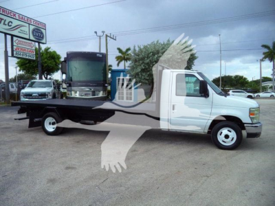 Flatbed tow truck on lot showing long wheelbase cab and power steel flatbed with side rails; dealership signage and other vehicles in background.