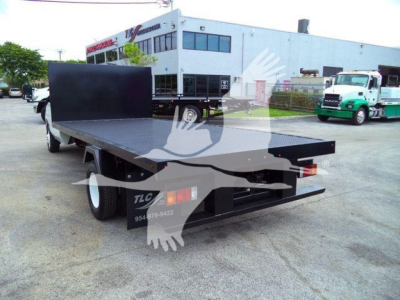 Flatbed tow truck bed on a Ford E-450, rear view showing flat platform and black metal side panels, generic dealership lot in background.