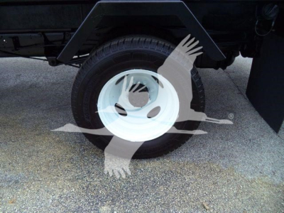 Wheel and tire on a Ford E-450 flatbed truck showing a white steel wheel with black tire and undercarriage components.