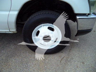 Front right wheel of a light-duty Ford E-450 flatbed truck showing steel rim and tire, partial front bumper.