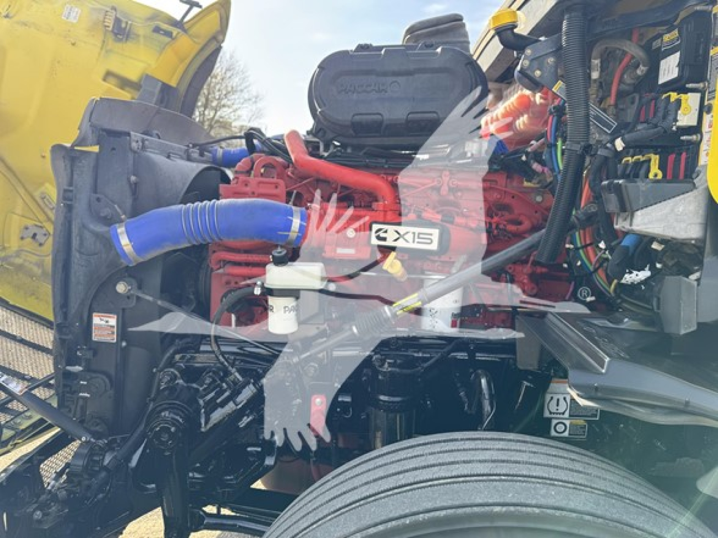 Peterbilt 579 engine bay with Exxis GX15 label visible on red engine component and blue radiator hose in foreground.