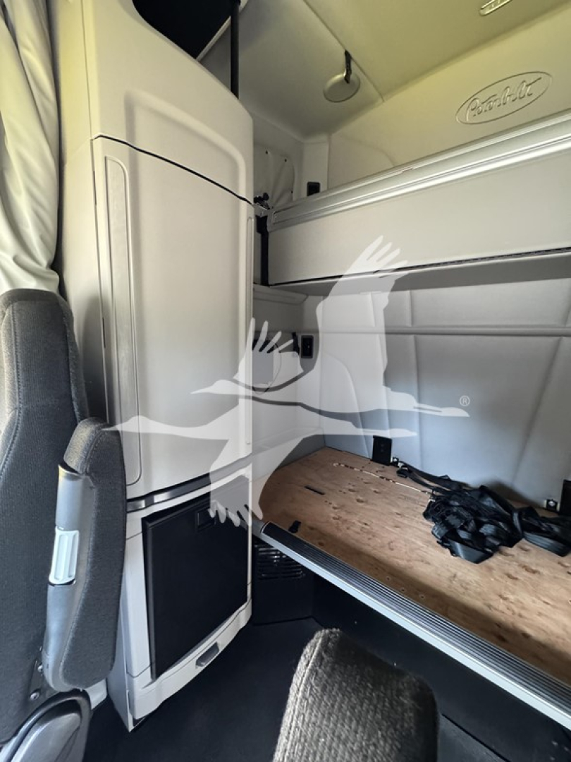 Truck cab interior showing sleeper area with a raised bunk, storage compartments, and a Peterbilt badge on the side panel.