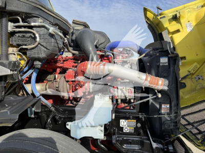 Peterbilt 579 engine bay view showing red engine, yellow cab, hoses, coolant reservoir, and various labels.