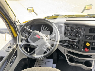 Truck cab interior from driver side showing steering wheel with Peterbilt emblem, instrument cluster, dash controls, and gear area.