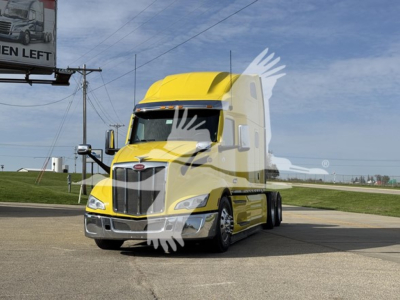 Peterbilt 579 conventional sleeper truck in yellow, front-and-side view, stock photo with dealership watermark and light reflections.