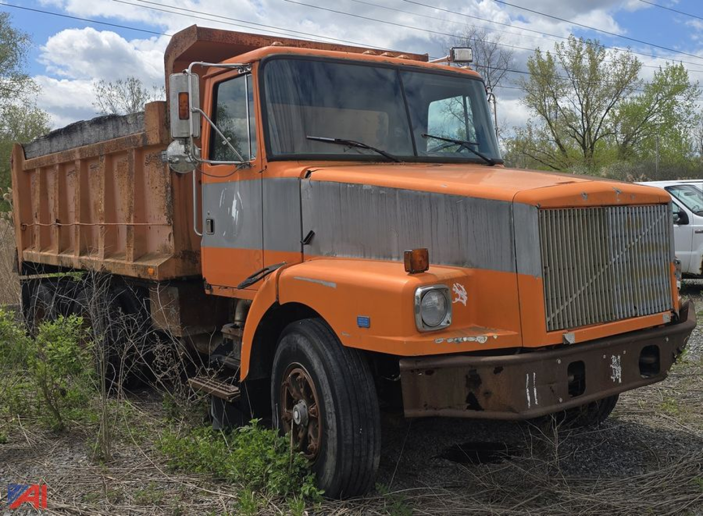 Dump truck showing orange cab with gray midsection and a large rectangular grille, front bumper, and bed in a field.