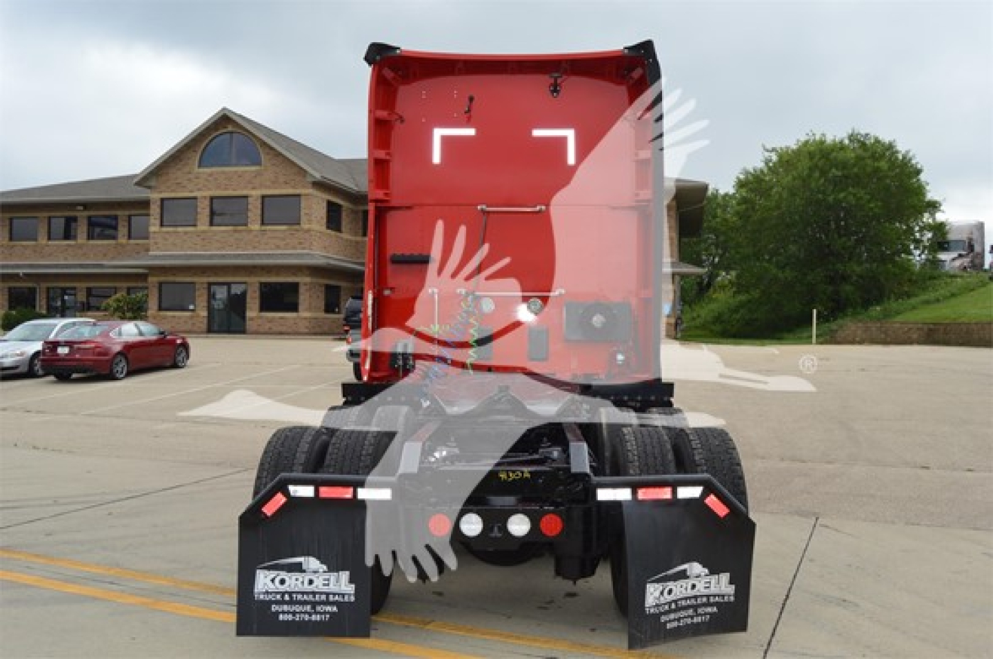 Rear view of a red Kenworth semi-truck sleeper with dual rear axles and mud flaps, in a parking lot.