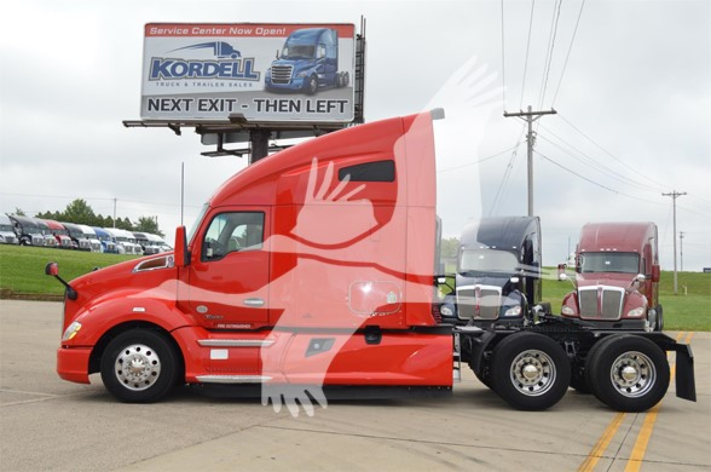 Kenworth T680 tractor with red cab and sleeper, side view showing wheels and fifth wheel; billboard in background reads 'KORDELL' and 'NEXT EXIT - THEN LEFT' with truck imagery.