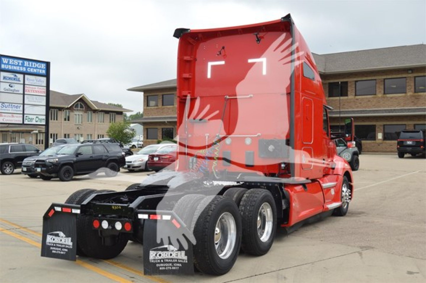 Red Kenworth T680 tractor in a parking lot, rear view showing fifth wheel and dual rear axles. Visible decals: none legible.