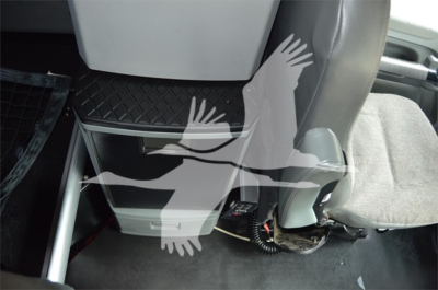 Cab interior of a 2018 Kenworth T680 showing a center console and lower dash area near the driver seat. Visible components include a cab floor, seat, and under-seat storage with wiring and a silver boxed cabinet.