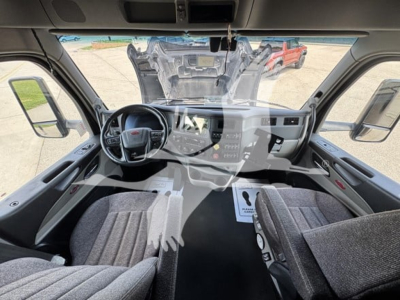 Truck cab interior of a 2023 Peterbilt 579, driver seat, steering wheel, dashboard, center console, seats, and windshield view of engine bay area reflected as overlay