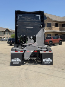 Rear view of a black Peterbilt 579 truck with open back cab, showing hoses and connectors, mud flaps with Kordell Truck & Trailer Sales branding, and dealership lot in background.