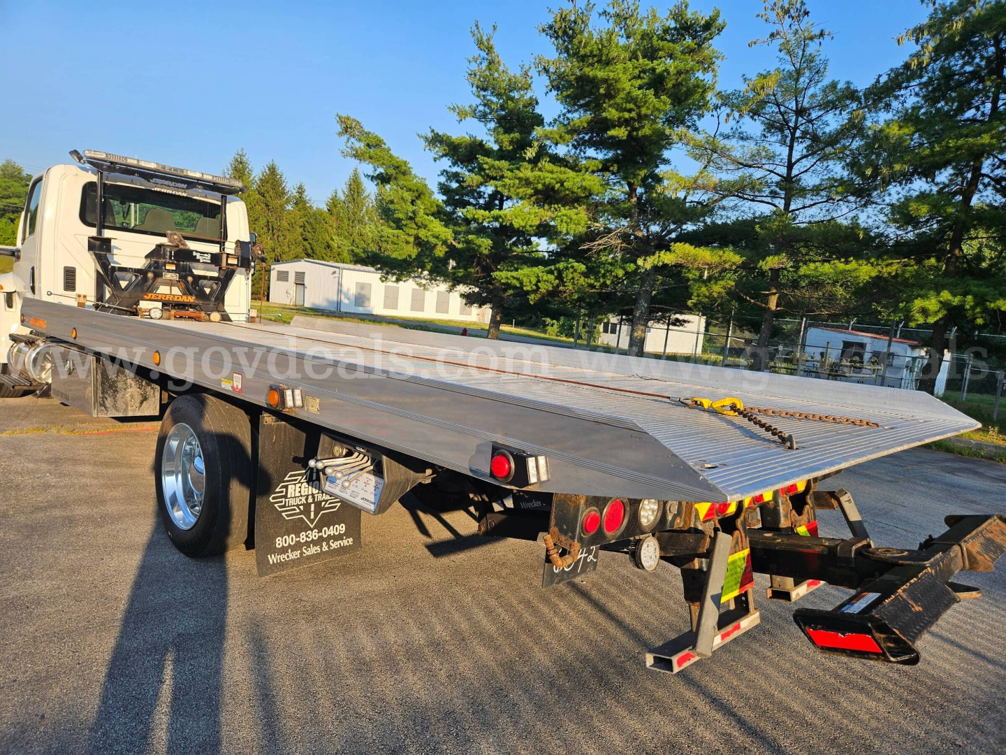 Flatbed tow truck with long metal deck and rear loading ramps, 2019 International MV607 vehicle in background, stock number 32136-38, VIN 1HTEUMML5KH242148.
