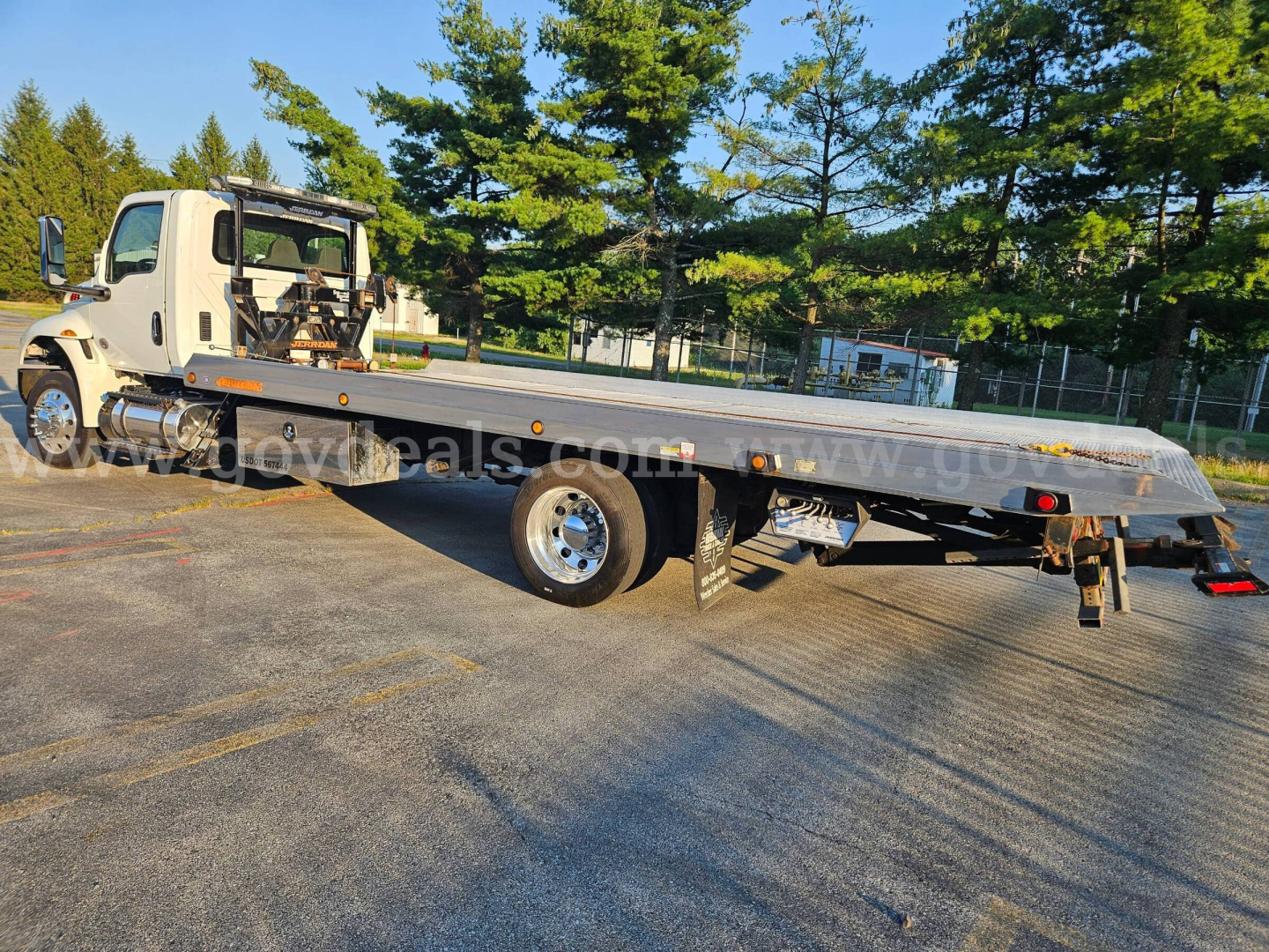 Flatbed tow truck with International MV series cab showing long wheelbase and wheel lift platform.